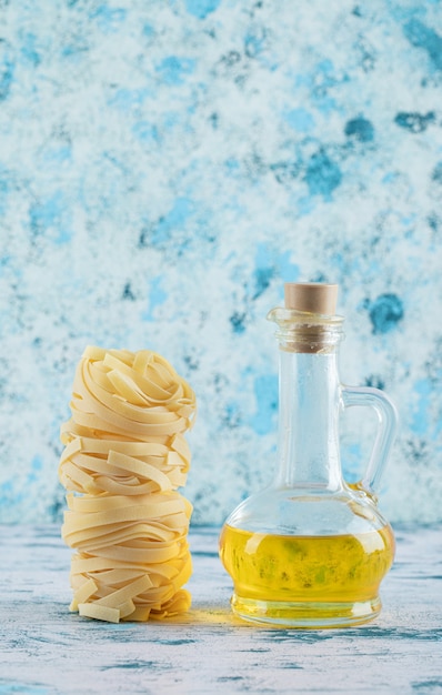 Foto gratuita pila de nidos de tagliatelle y vaso de aceite de oliva en azul.