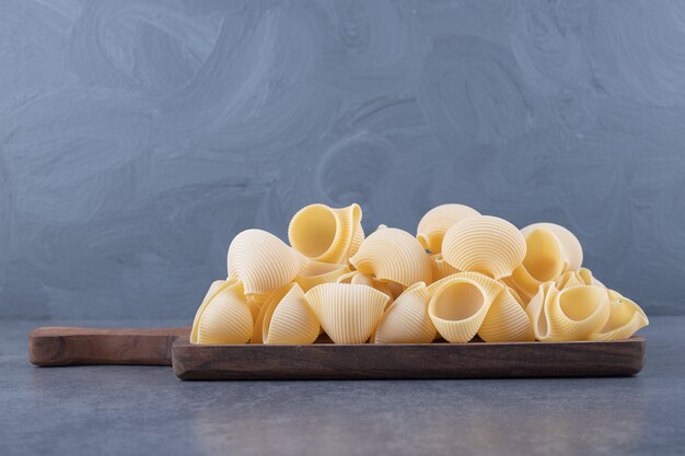 Pila de pasta conchiglie sobre tabla de madera.