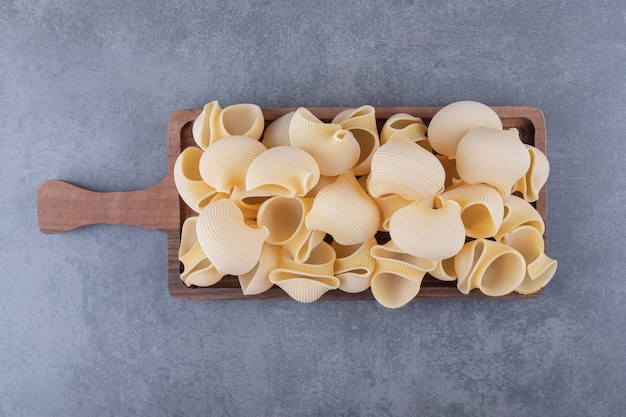 Pila de pasta conchiglie sobre tabla de madera.