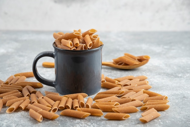 Pila de pasta dietética marrón con taza negra sobre superficie gris.