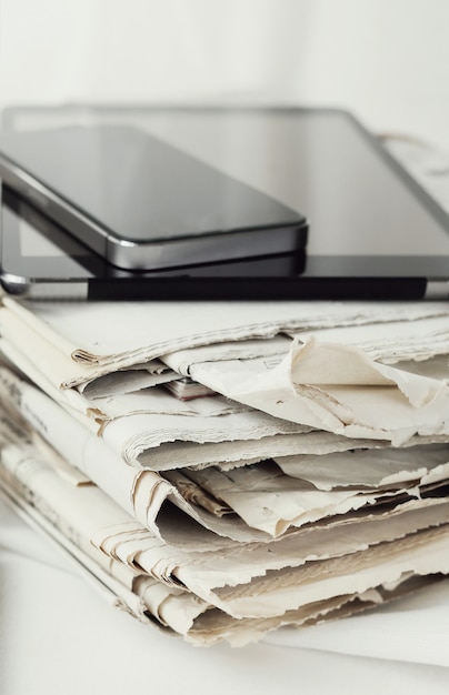 Pila de periódicos con tableta digital y teléfono inteligente
