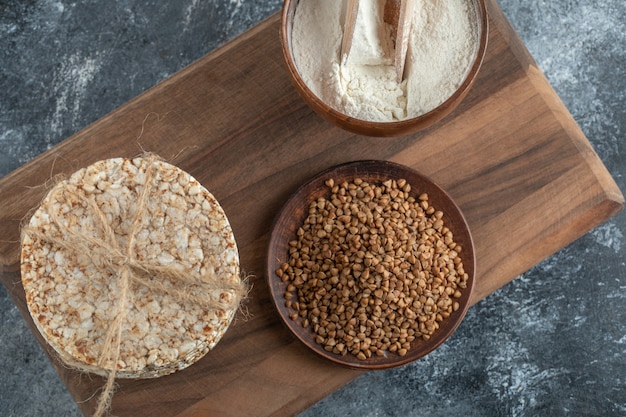 Pila de tortas de arroz, tazón de harina y trigo sarraceno sobre tabla de madera