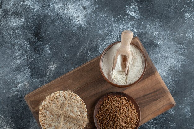 Pila de tortas de arroz, tazón de harina y trigo sarraceno sobre tabla de madera