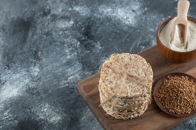 Pila de tortas de arroz, tazón de harina y trigo sarraceno sobre tabla de madera