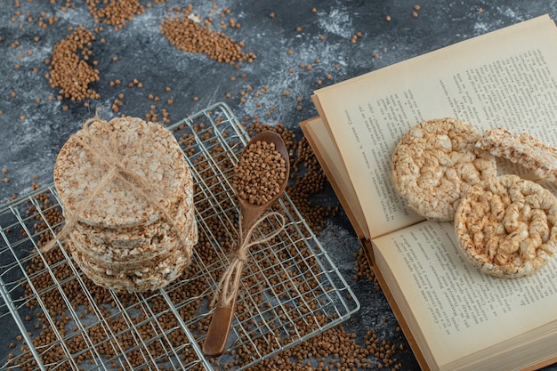 Pila de tortas de arroz, trigo sarraceno y libro sobre superficie de mármol