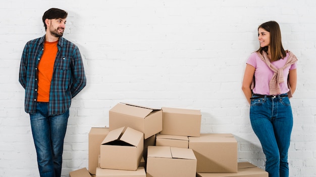 Pilas de cajas de cartón entre la pareja joven y elegante de pie contra la pared mirando a la cámara