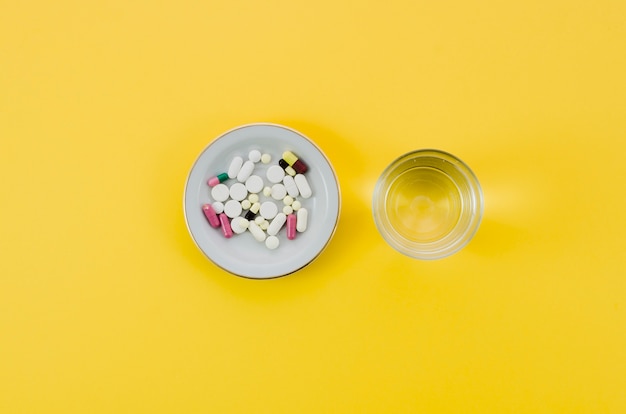 Píldoras médicas en agua del tazón y del vidrio en fondo amarillo