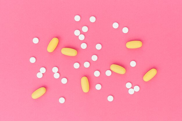 Píldoras médicas blancas y amarillas en fondo rosado