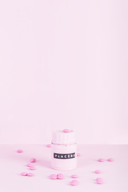 Las píldoras rosadas rodeadas con placebo cerraron la botella sobre fondo rosado