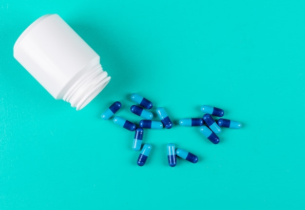 Píldoras de la vista superior con frasco de pastillas abierto sobre fondo azul cian. espacio horizontal para texto