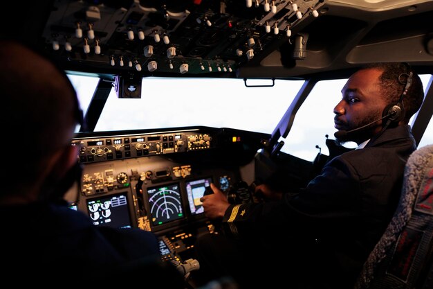 Piloto afroamericano que vuela un avión haciendo trabajo en equipo con el capitán, usando el comando y la navegación del tablero. Equipo de aviones empujando los botones del panel de control y la palanca para despegar y volar.