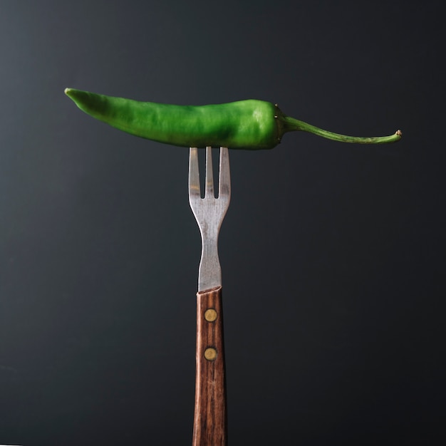 Pimienta de chile verde en tenedor sobre fondo negro