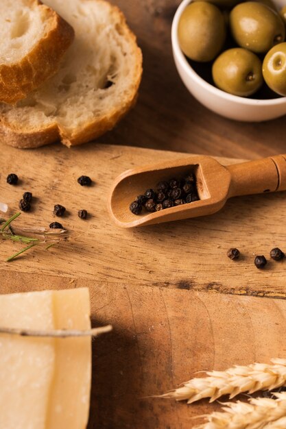 Pimienta negra en tabla de cortar con aceitunas y parmesano