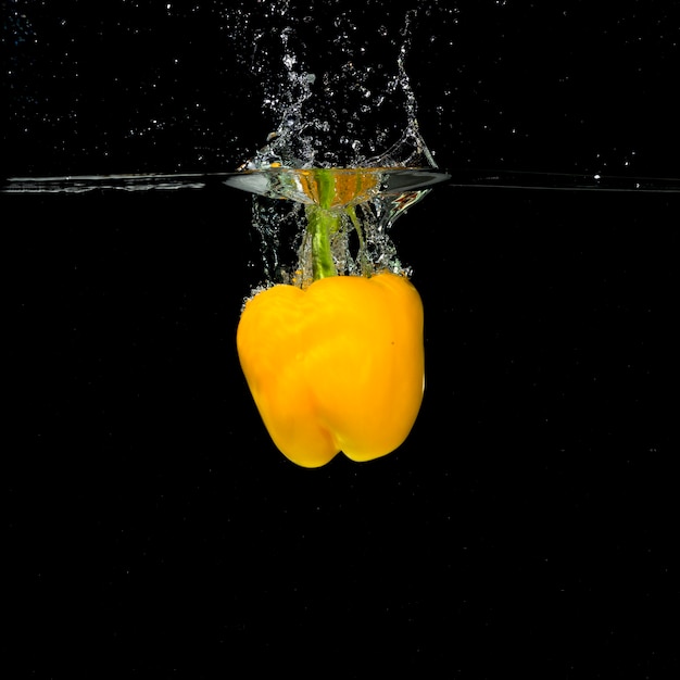 Pimiento amarillo salpicaduras en el agua sobre fondo negro