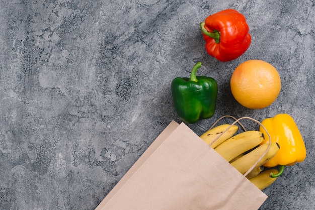 Pimiento colorido; Naranja y plátanos sobre fondo gris de hormigón