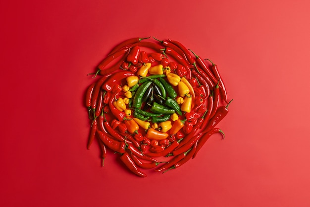 Pimiento rojo amarillo y verde dispuestas en círculo sobre fondo rojo. Verduras frescas de colores. Vista de ángulo alto. Diseño creativo. Chile picante condimentado. Concepto de dieta vegetariana. Gran variedad