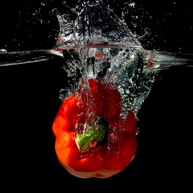 Pimiento rojo cayendo en agua sobre fondo negro