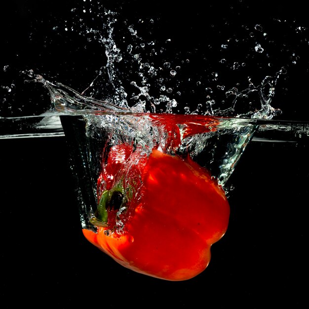 Pimiento rojo fresco cayendo en el agua con splash sobre fondo negro