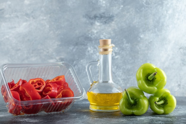 Foto gratuita pimiento rojo en rodajas en un recipiente de plástico con pimiento verde y una botella de aceite sobre fondo gris