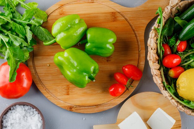 Pimiento verde en una tabla de cortar con tomates, sal, queso, limón vista superior sobre una superficie gris