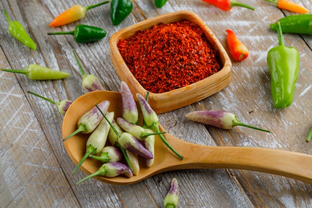 Pimientos en una cuchara de madera con escamas de pimiento rojo vista de ángulo alto en una madera