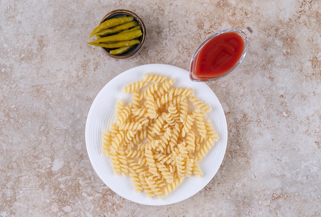 Pimientos en escabeche, salsa de tomate y macarrones en superficie de mármol.
