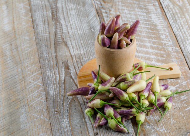 Pimientos en un florero sobre tabla de cortar y madera, vista de ángulo alto.