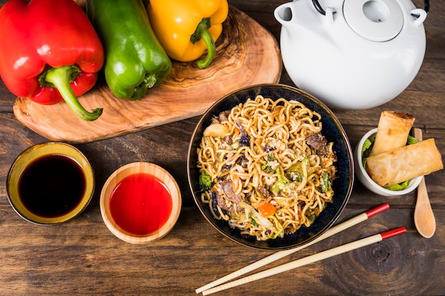 Pimientos; pasta Udon; Salsas y rollitos de primavera en escritorio blanco