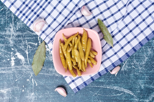 Pimientos picantes en escabeche en un plato con hojas, ajo y mantel.