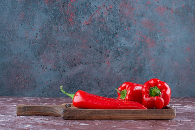 Pimientos picantes y morrones en una tabla, sobre el fondo de mármol.