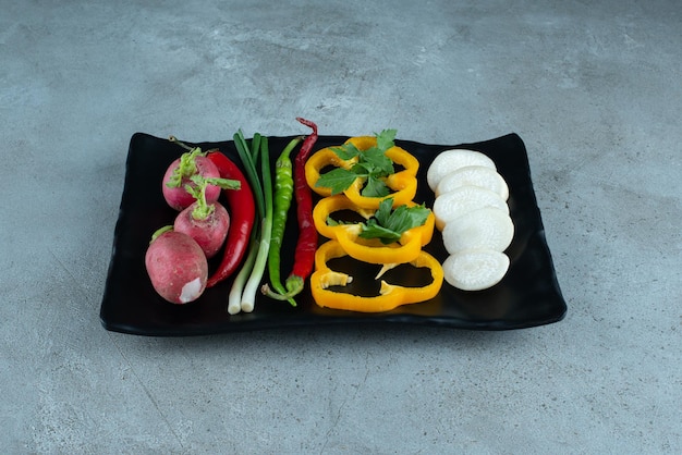 Pimientos en rodajas, nabos, verduras y cebollas en un plato negro.