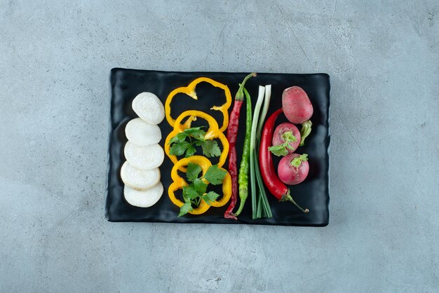 Pimientos en rodajas, nabos, verduras y cebollas en un plato negro.