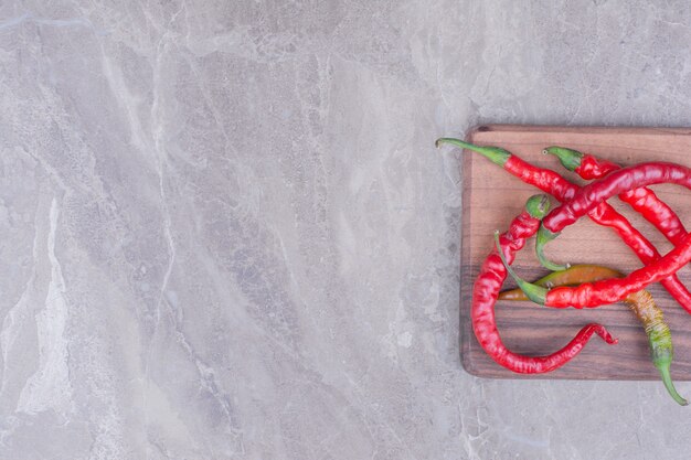 Pimientos rojos aislados en una tabla de madera sobre la superficie de mármol