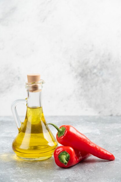 Pimientos rojos con una botella de aceite de oliva virgen extra sobre mesa de mármol.
