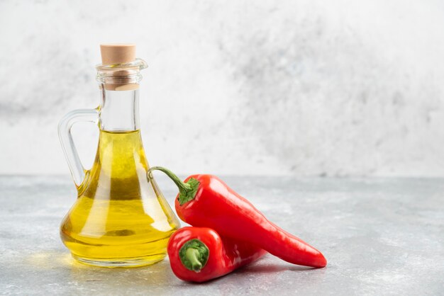 Pimientos rojos con una botella de aceite de oliva virgen extra sobre mesa de mármol.