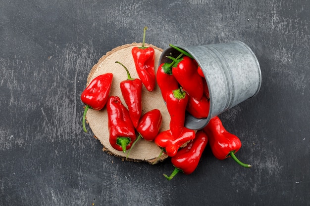 Pimientos rojos dispersos de un mini cubo con vista superior de pieza de madera en una pared gris sucio