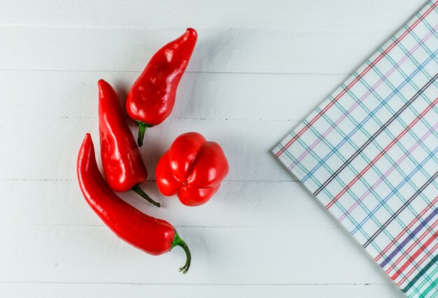 Pimientos rojos con papel de cocina sobre una superficie de madera blanca, plana.