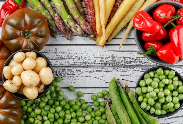 Pimientos rojos con patatas, tomates, espárragos, vainas verdes, guisantes, zanahorias en un recipiente en la pared de madera, vista superior.