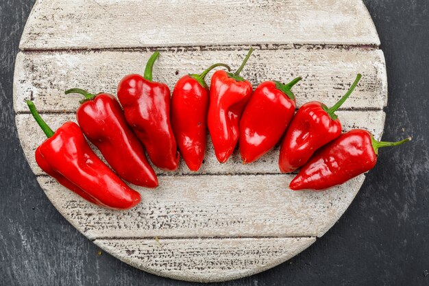 Pimientos rojos en una pieza de madera en una pared oscura del grunge. aplanada