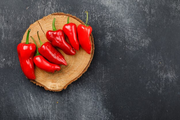 Pimientos rojos en una pieza de madera en una pared oscura del grunge. vista superior.