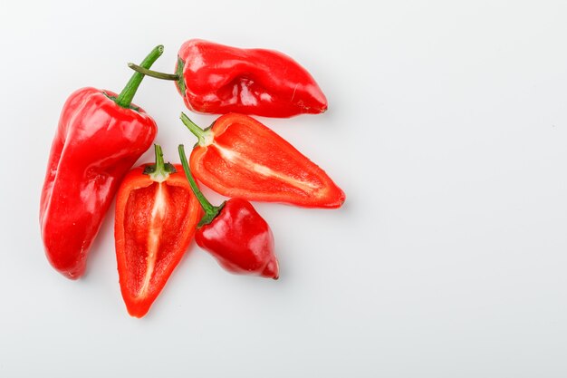 Pimientos rojos con rodajas en la pared blanca, endecha plana.