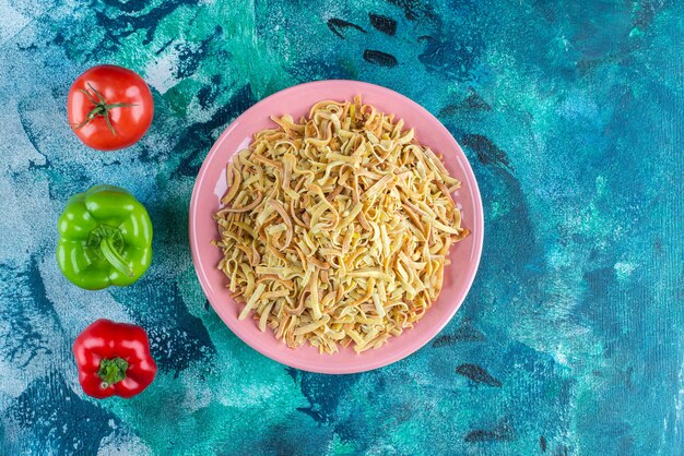 Pimientos, tomates y fideos en un plato, sobre la mesa azul.