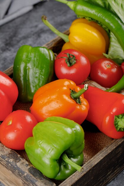 Pimientos y tomates frescos coloridos en una bandeja rústica.