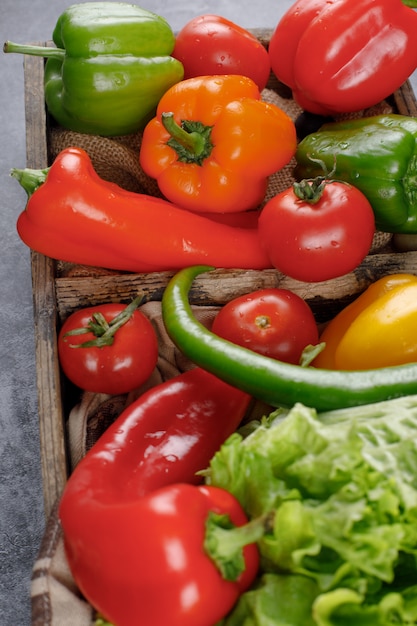 Pimientos, tomates y vegetación en un recipiente de madera. Vista superior.