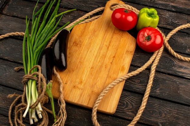 Pimientos verdes berenjenas negras maduras frescas tomates rojos junto con verduras en un piso rústico de madera marrón