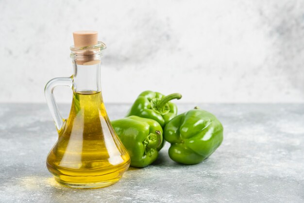 Pimientos verdes con una botella de aceite de oliva virgen extra sobre mesa de mármol.