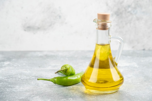 Pimientos verdes con una botella de aceite de oliva virgen extra sobre mesa de mármol.