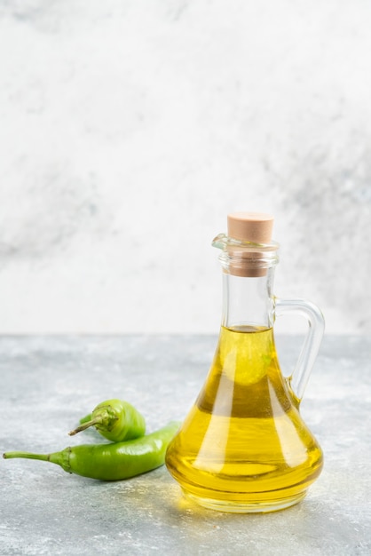 Pimientos verdes con una botella de aceite de oliva virgen extra sobre mesa de mármol.