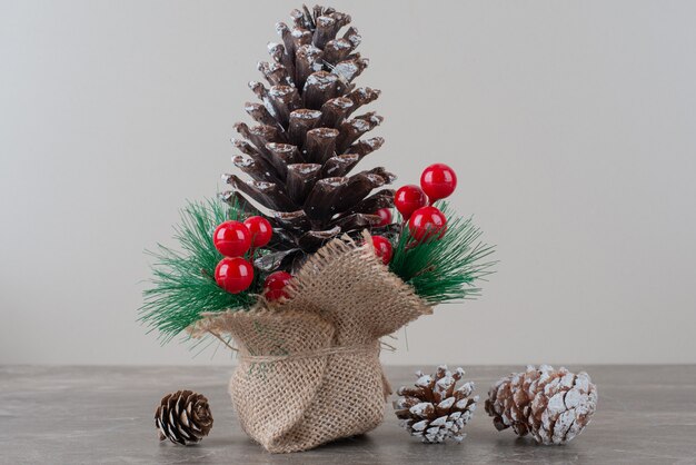 Piña decorada con bayas de acebo y ramas sobre mesa de mármol.