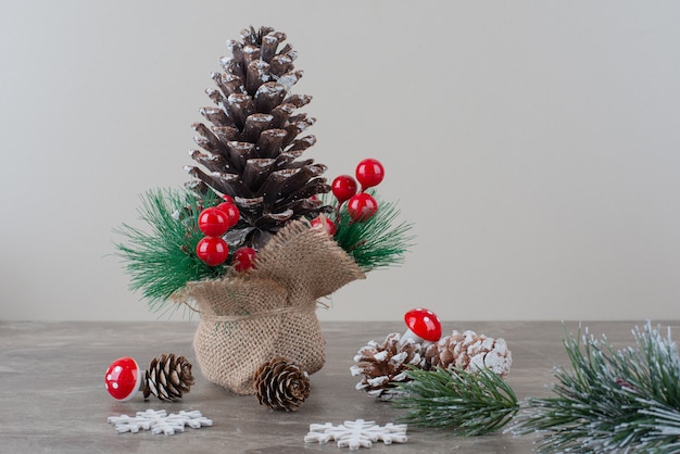 Piña decorada con bayas de acebo y ramas sobre mesa de mármol.